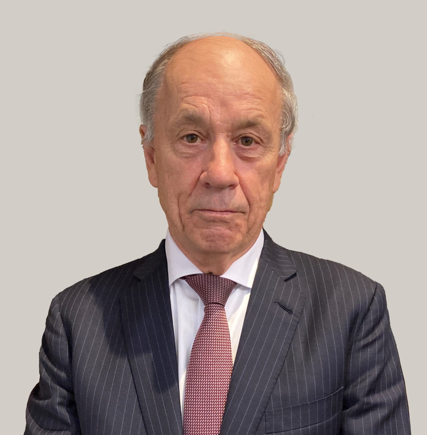 Man in pinstripe suit, white shirt, and patterned red tie on gray background.